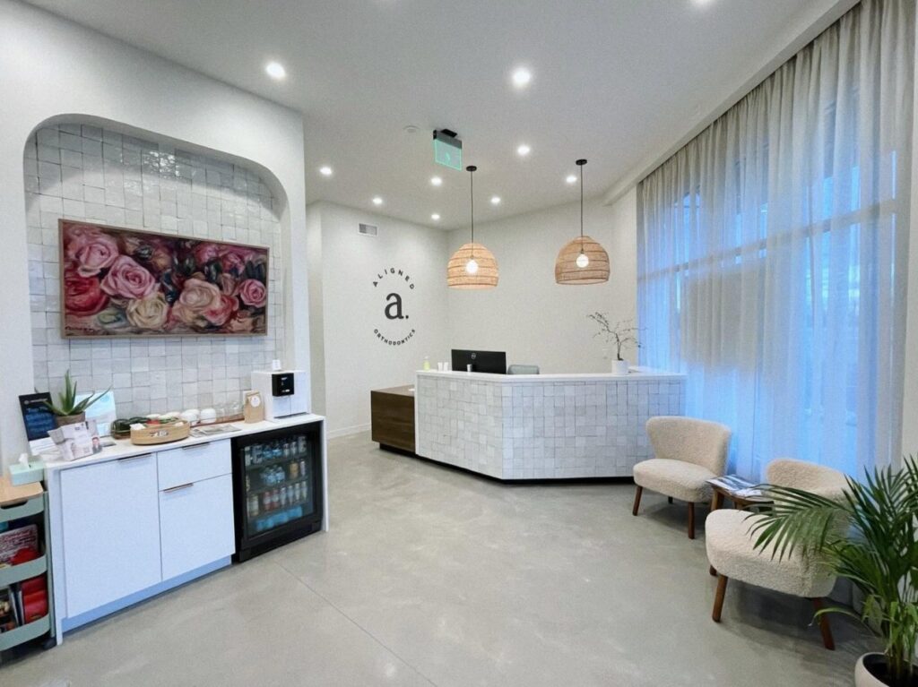 Bright waiting room at Aligned Orthodontics on South Pearl Street with a white tile front desk and a beverage bar