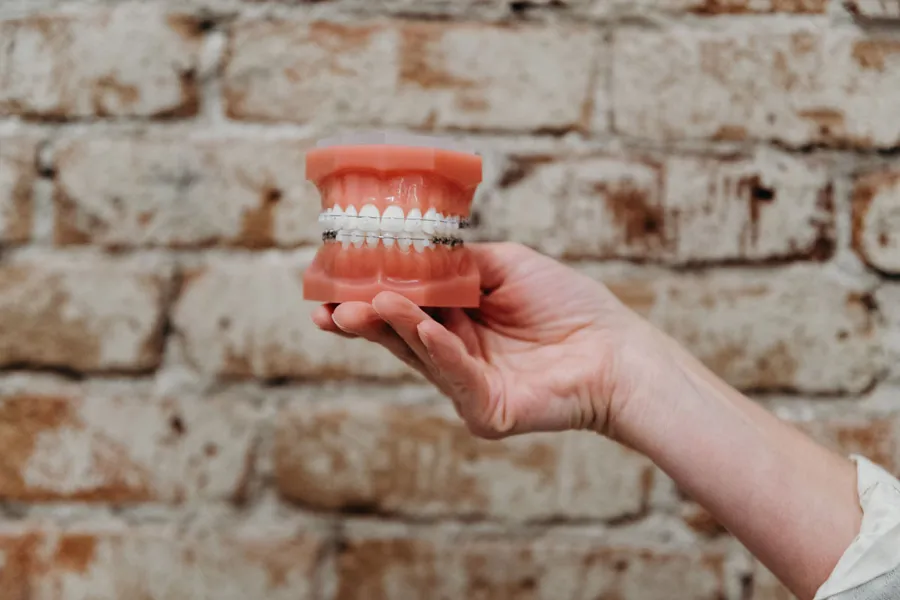 Teeth model with tooth-colored clear braces held in front of a brick wall in Denver